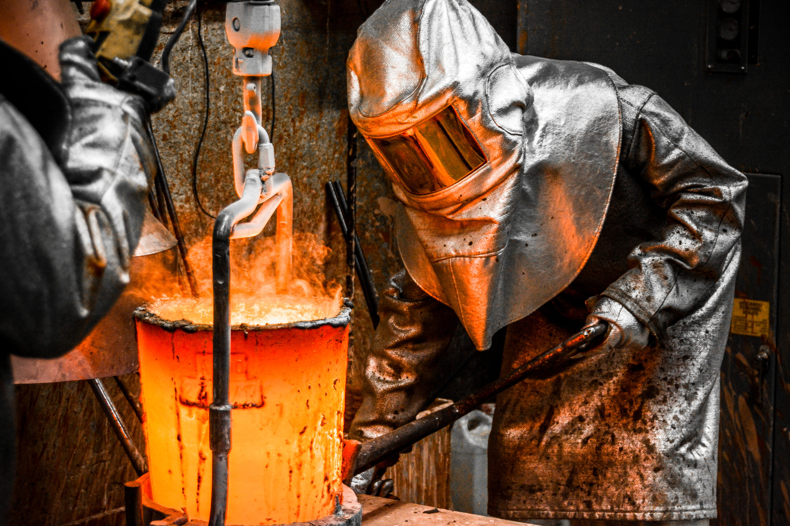 In a foundry workshop. Workers protected by their safety equipment handle a crucible containing molten metal