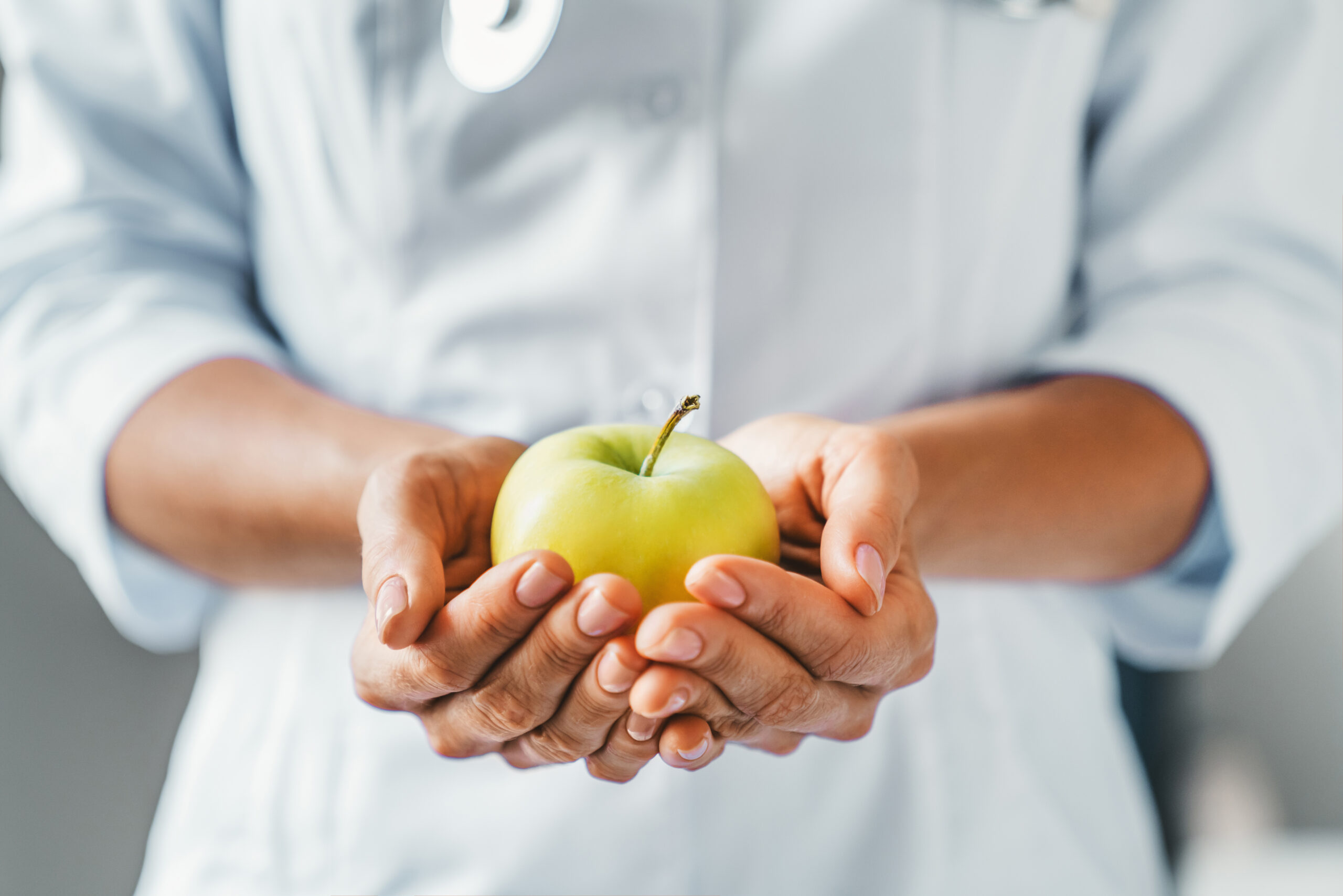 Cropped shot of female doctor holding apple with both hand in clinic